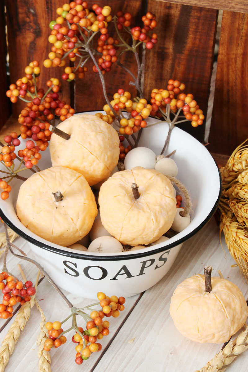 Handmade pumpkin soaps in a white enamel bowl surrounded by fall branches.