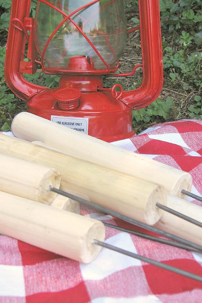 Metal skewers and wood dowels to make custom roasting sticks on a red and white checkered cloth.