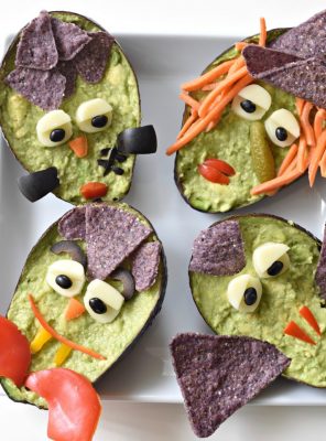 Guacamole monsters in an avocado decorated with a variety of vegetables.