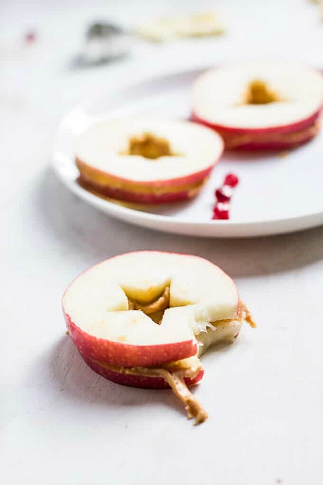 Apple slices with cookie cutter cut-outs and nut butter for a healthy Christmas snack.