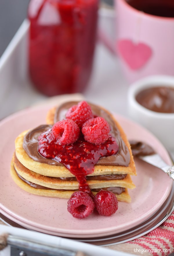 Heart shaped pancakes with Nutella and homemade raspberry sauce on a pink plate for Valentine's Day.