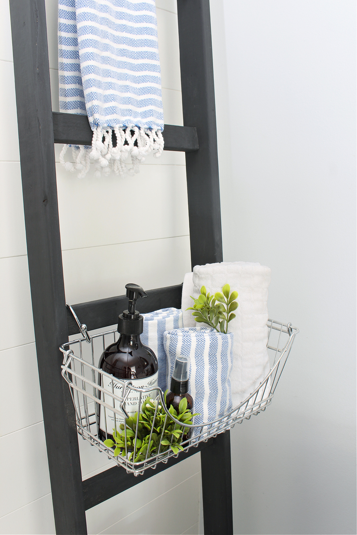Black DIY bathroom storage ladder with wire baskets.