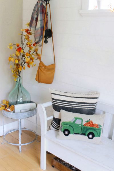 Fall front entryway decorated for fall with faux leaves and a fall pillow.