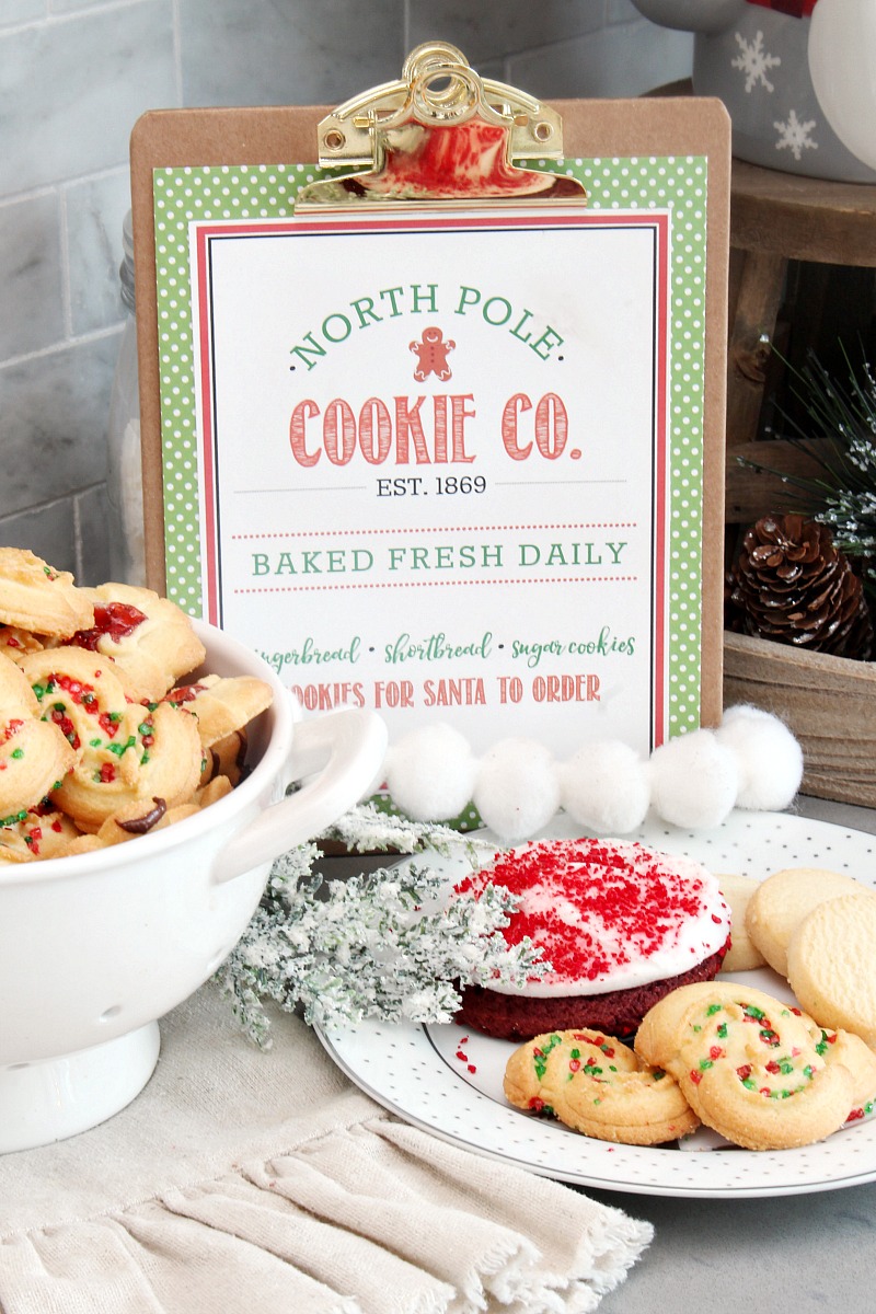 North Pole Cookie Co. free Christmas printable displayed on a clipboard with Christmas cookies.