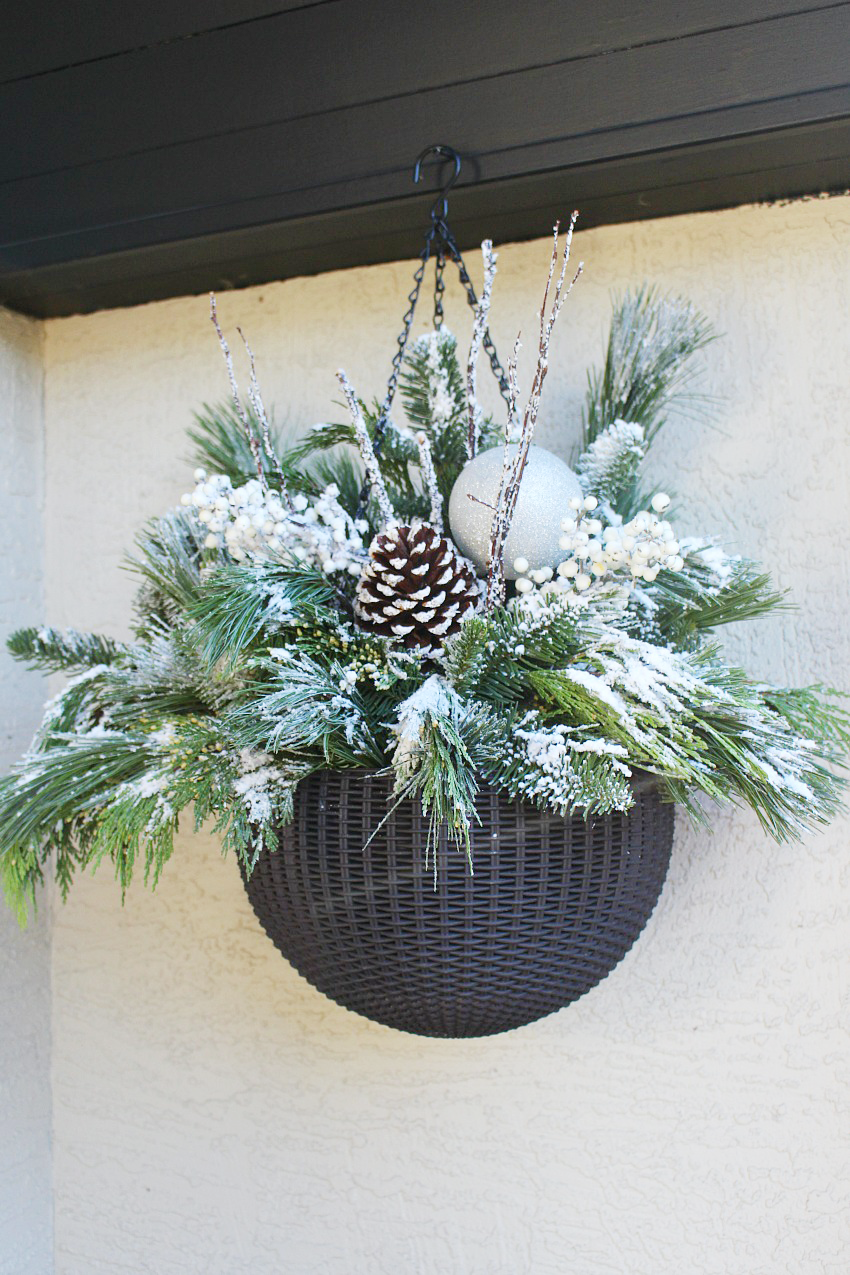 Quick and easy DIY outdoor hanging baskets. A mix of fresh greenery, pinecones, and berries with a light flocking of snow.