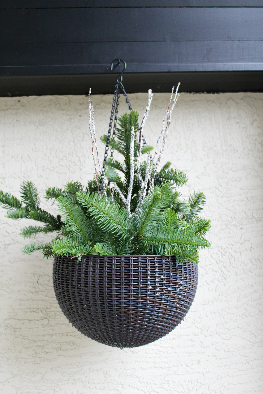 Quick and easy DIY outdoor hanging baskets. A mix of fresh greenery, pinecones, and berries with a light flocking of snow.