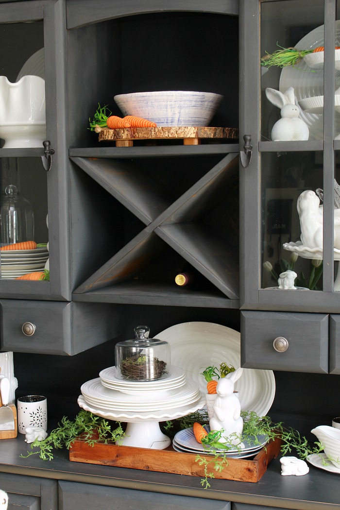 Black painted hutch decorated for Easter with white tableware and white ceramic bunnies.