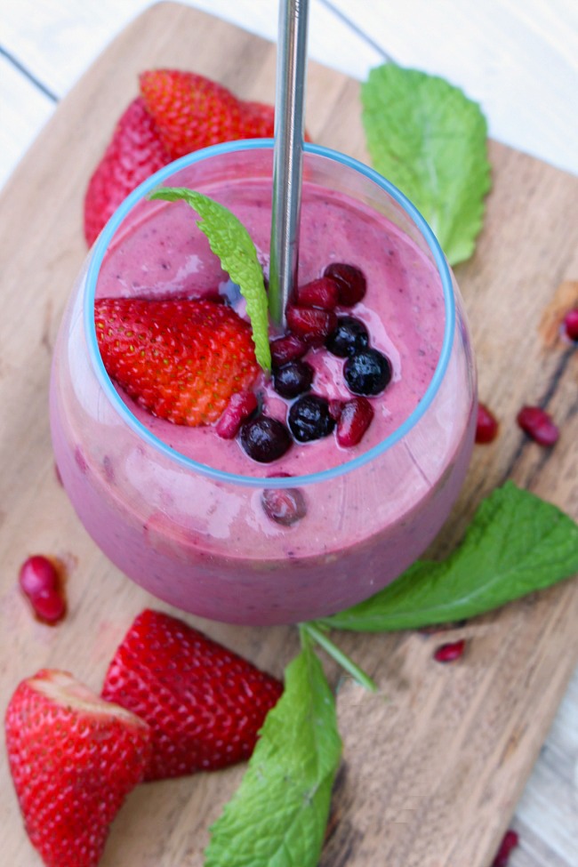 Berry green smoothie with blueberries, strawberries, pomegranate seeds for garnish.