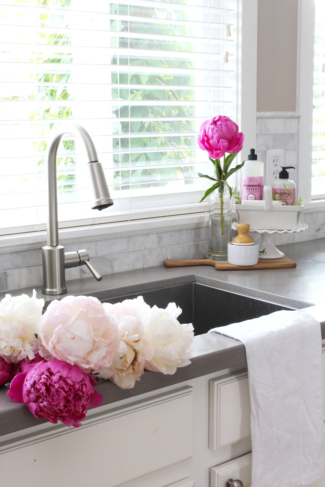 White farmhouse style kitchen with beautiful pink peonies in the sink. 