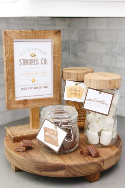 Campfire S'mores Printable in a wooden frame with s'mores ingredients in labeled mason jars.