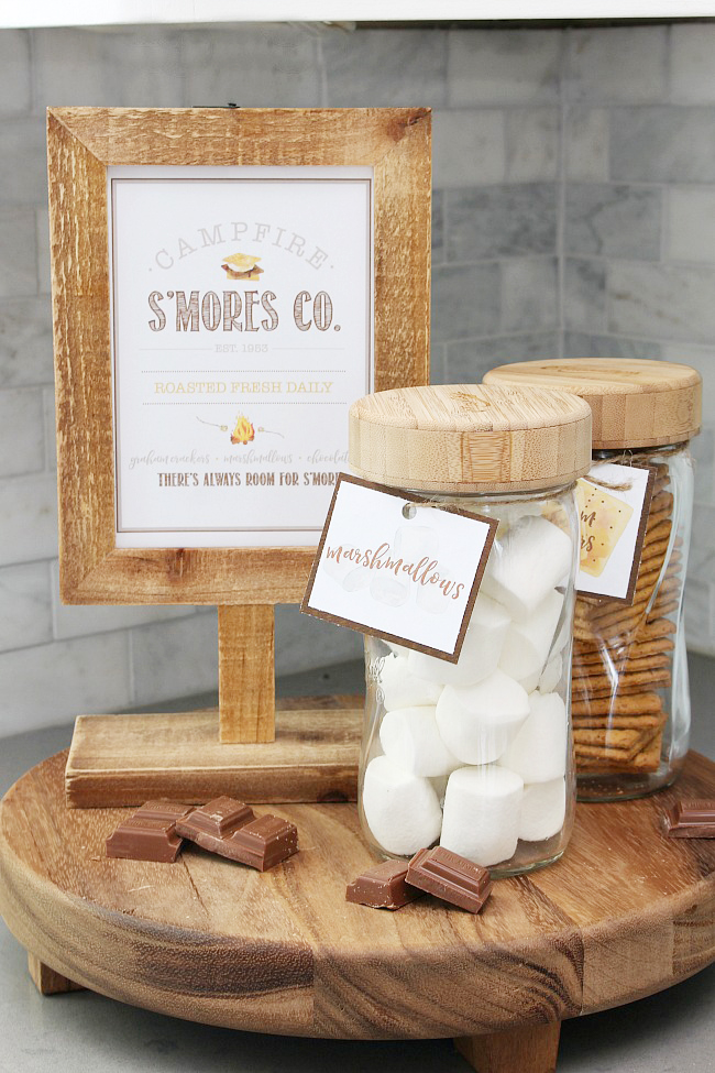 Campfire S'mores Printable in a wooden frame with s'mores ingredients in labeled mason jars.