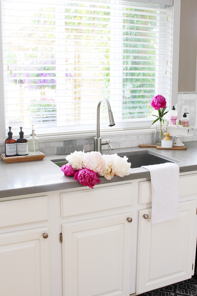 White farmhouse style kitchen with beautiful pink peonies in the sink.