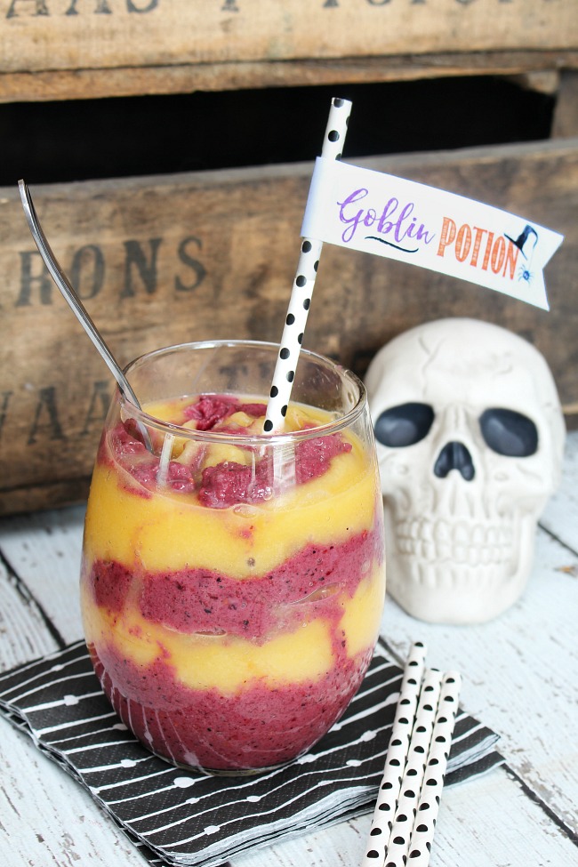 Orange and purple Halloween goblin potion smoothie in a clear glass with a fun straw topper.