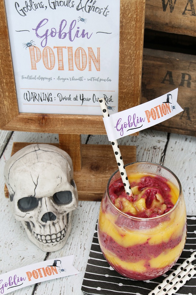 Goblin potion Halloween smoothie. Orange and purple smoothie layers swirled together for a tasty and healthy Halloween treat. Served in a clear glass with a goblin potion straw topper.