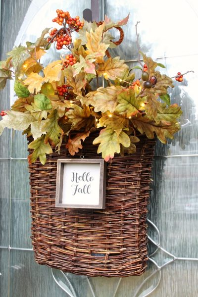 Fall basket wreath. Wicker basket filled with a variety of fall stems and mini lights. A wood "hello fall" sign is attached to the front.