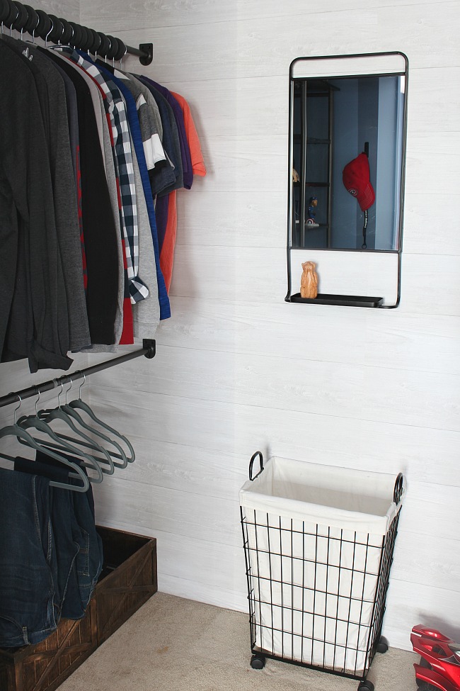 Organized kids closet with a closet organizer system, wire laundry basket, and black framed mirror.