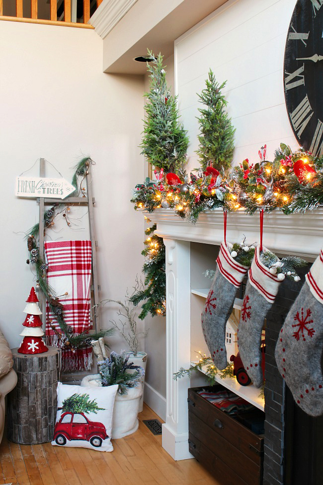 Christmas mantel decorated with garland, lights, Christmas trees, and traditional Christmas colors.