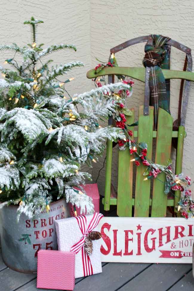 Christmas front porch with flocked tree in a galvanized metal bucket and a vintage sled with pretty wrapped presents.