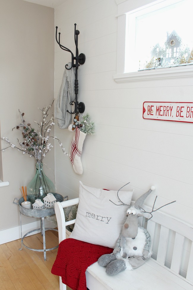 Farmhouse style front entryway with shiplap wall all decorated for Christmas with neutrals and pops of red.