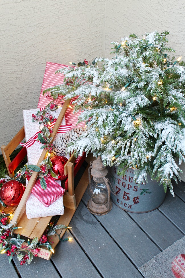 Christmas front porch with flocked tree in a galvanized metal bucket and a vintage sled with pretty wrapped presents.