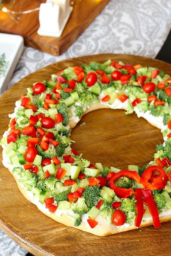 Christmas wreath veggie pizza on a wooden cutting board.
