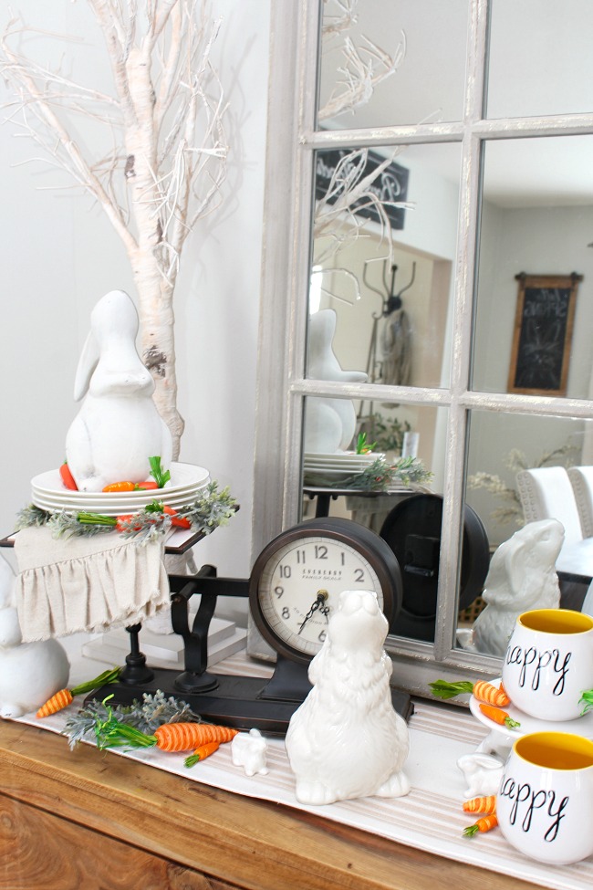 Dining room sideboard decorated for spring and Easter with white bunnies and carrots.