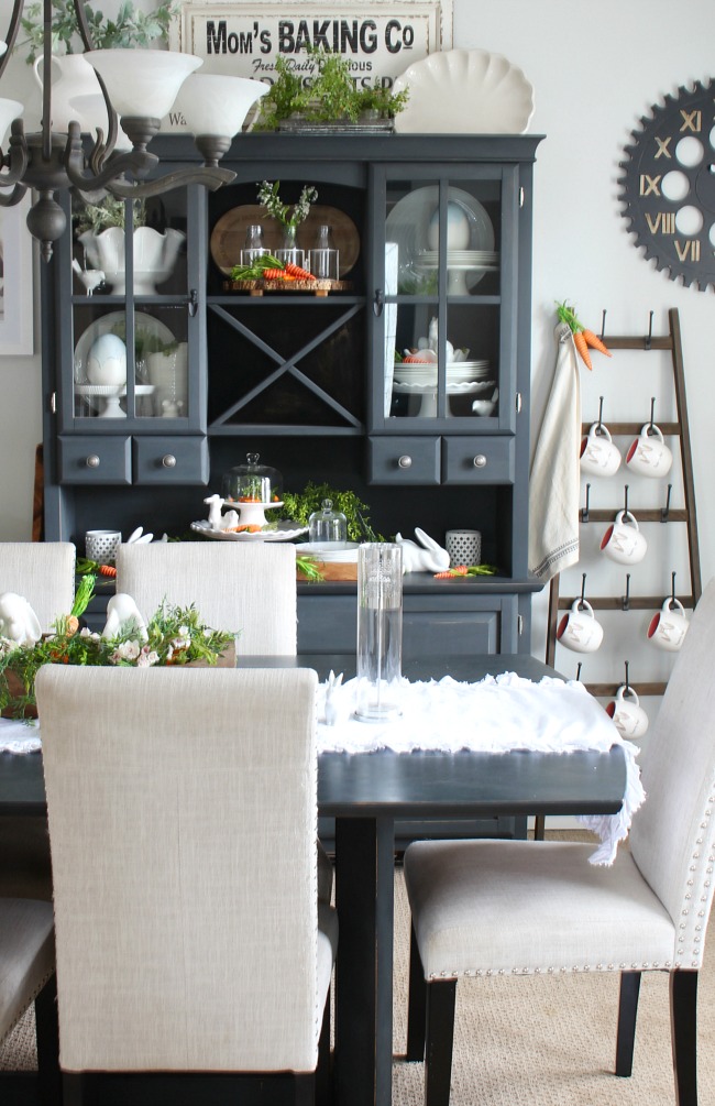 Farmhouse style dining room decorated for spring. Painted black table and buffet and hutch decorated with white and pops of orange. 