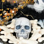 Meringue bones Halloween treats on a black plate with skull.