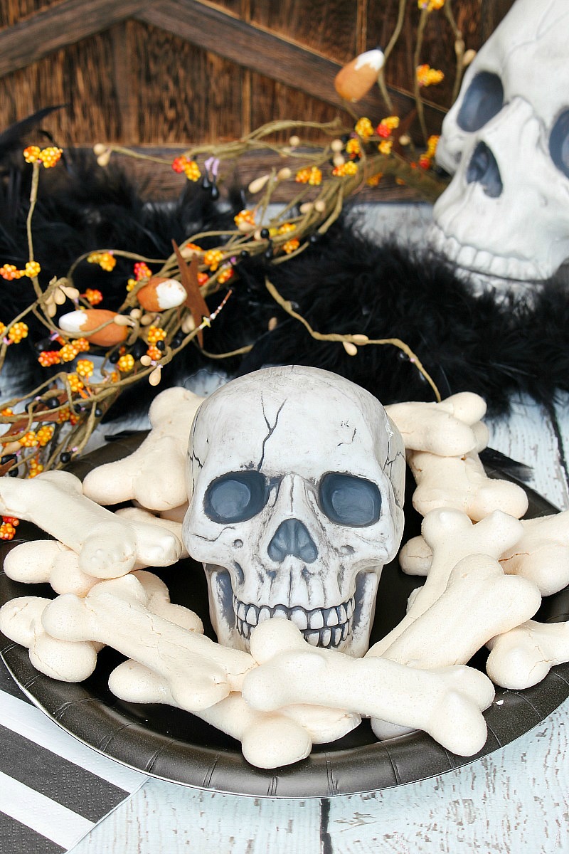 Meringue bones Halloween treats on a black plate with skull.