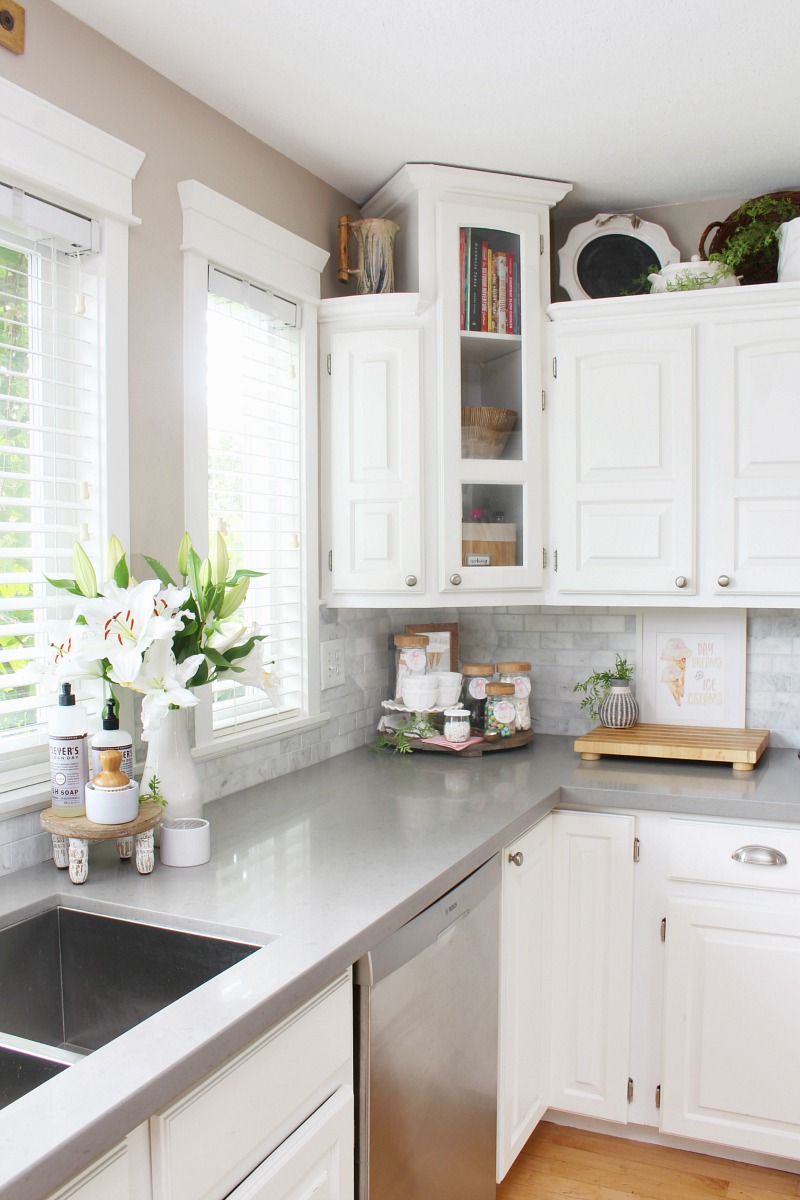 آشپزخانه سفید با میزهای کوارتز خاکستری که برای تابستان تزئین شده است.
