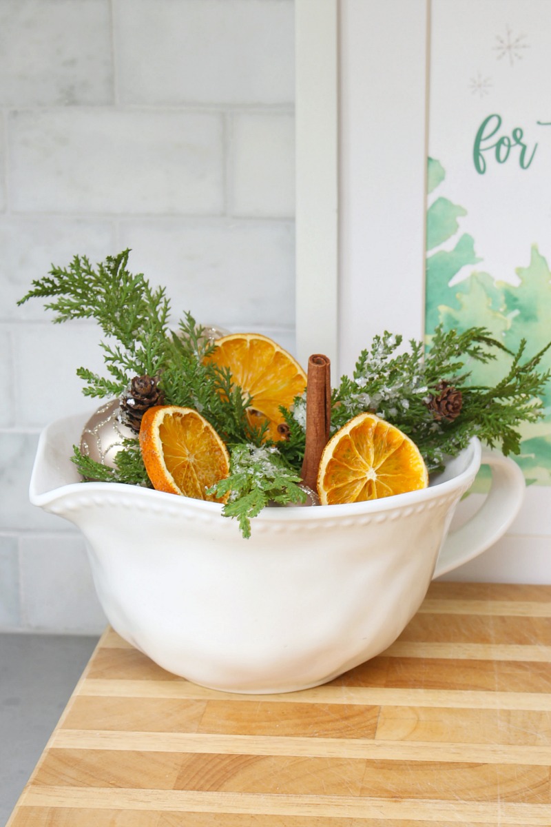 Dried orange slices in a bowl with greenery and Christmas ornaments.