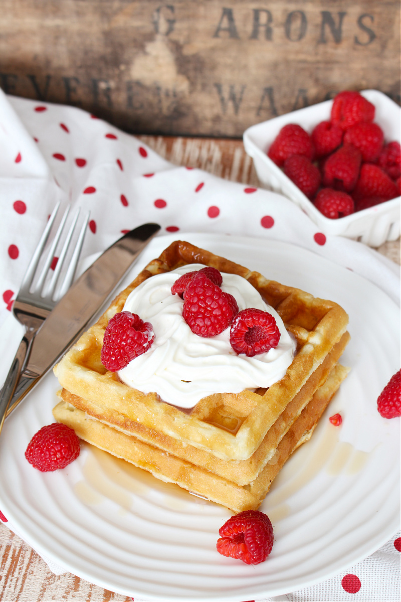 Belguim waffles with whipping cream, syrup, and raspberries.