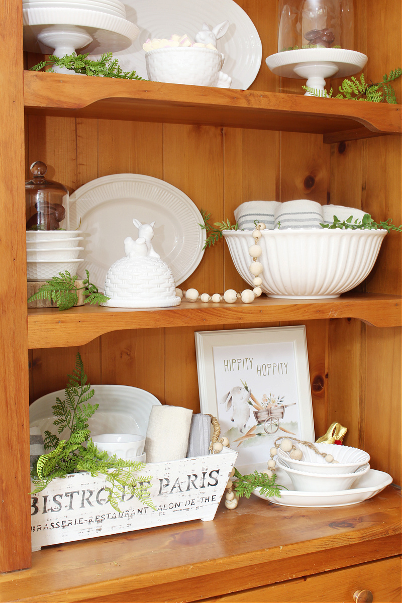 Wood hutch decorated for Easter with white dishware and white bunnies. 