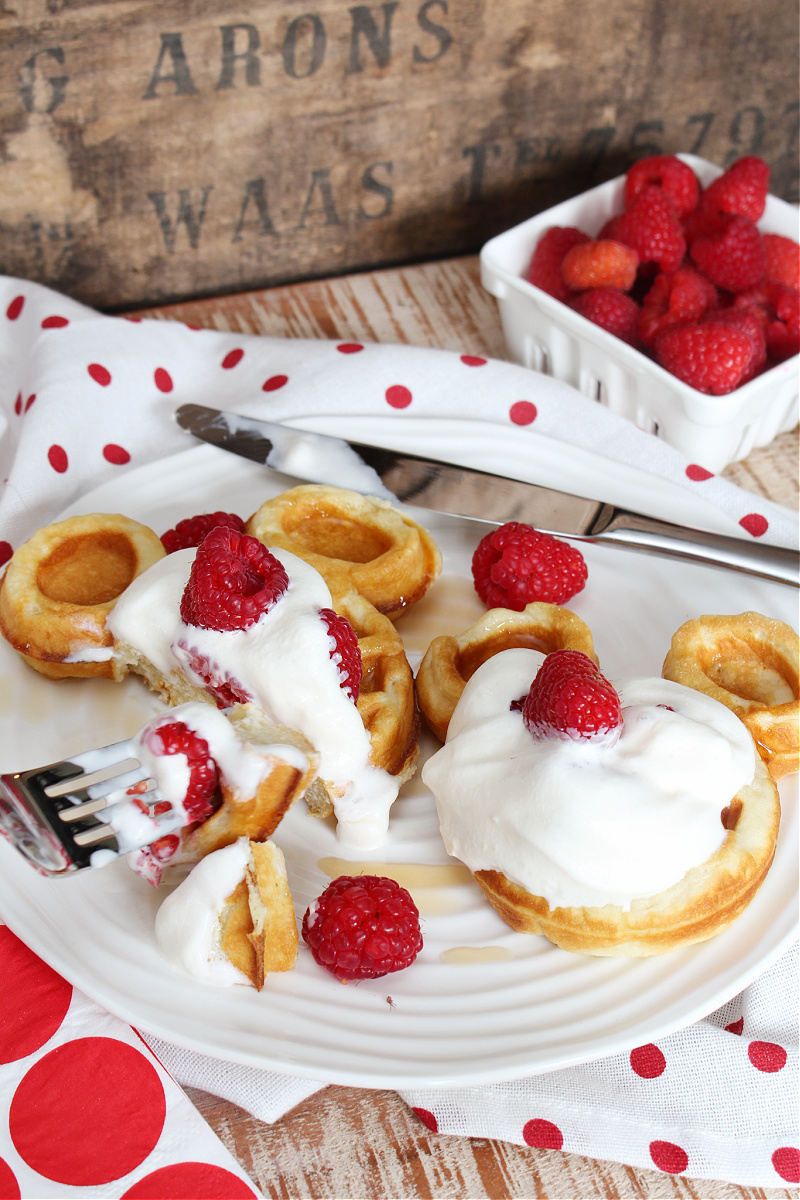 Cute Mickey Mouse waffles with whipping cream, syrup, and raspberries.