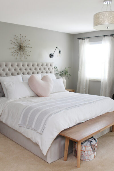 Grey upholstered bed with white bedding and a heart pillow.
