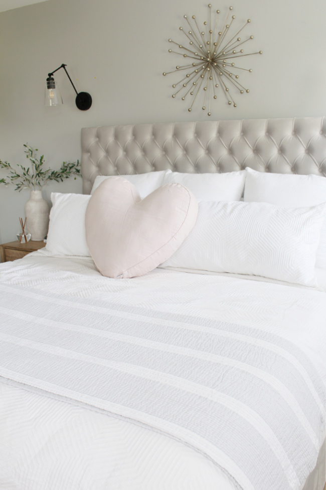 Upholstered bed with white bedding and a pink linen heart pillow.