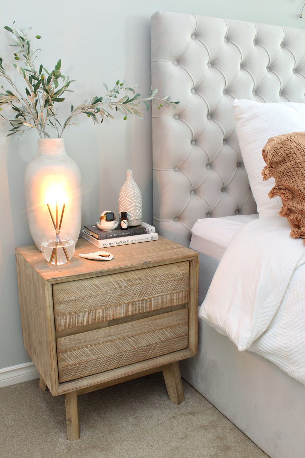 A nightstand with a candle next to an upholstered bed.
