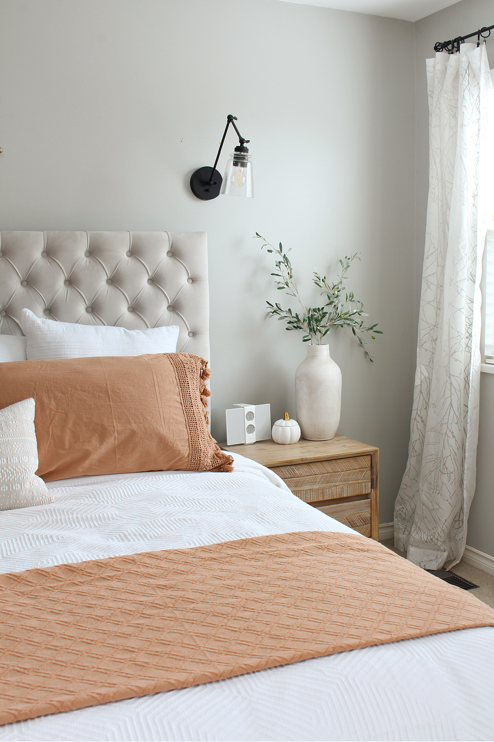 Upholstered bed dressed up for fall with a white duvet and terra cotta quilt and shams.