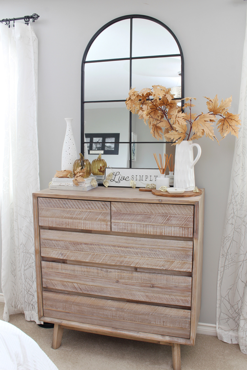 Bedroom dresser with a black arched mirror decorated for fall with neutral tones.