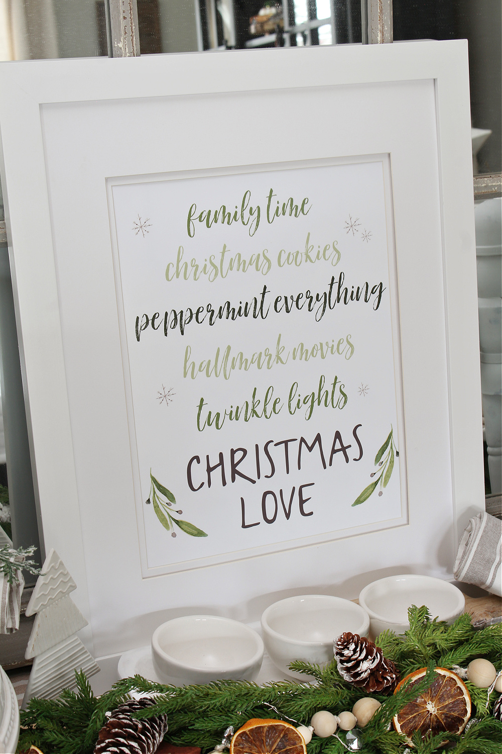 Christmas Love Christmas printable in a frame on a Christmas sideboard.