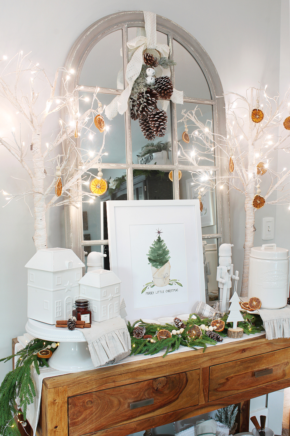 Sideboard decorated with free Christmas printable, greenery, and dried oranges.