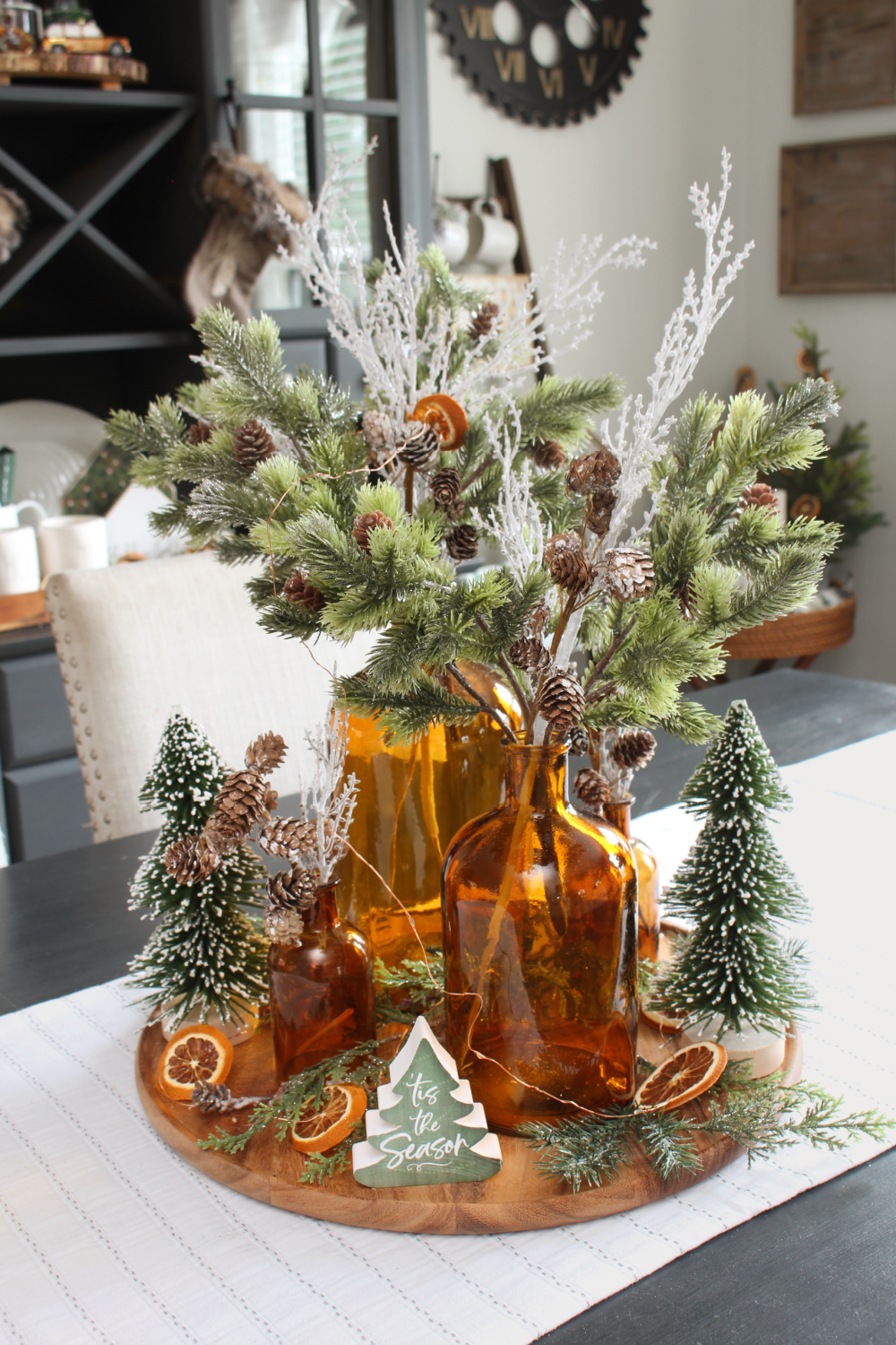 Beautiful Christmas centerpiece with amber glass bottles, greenery, and dried oranges.