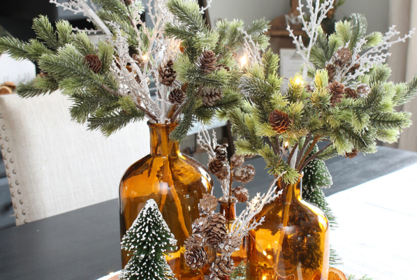 Pretty lighted Christmas centerpiece with amber glass bottles and greenery.