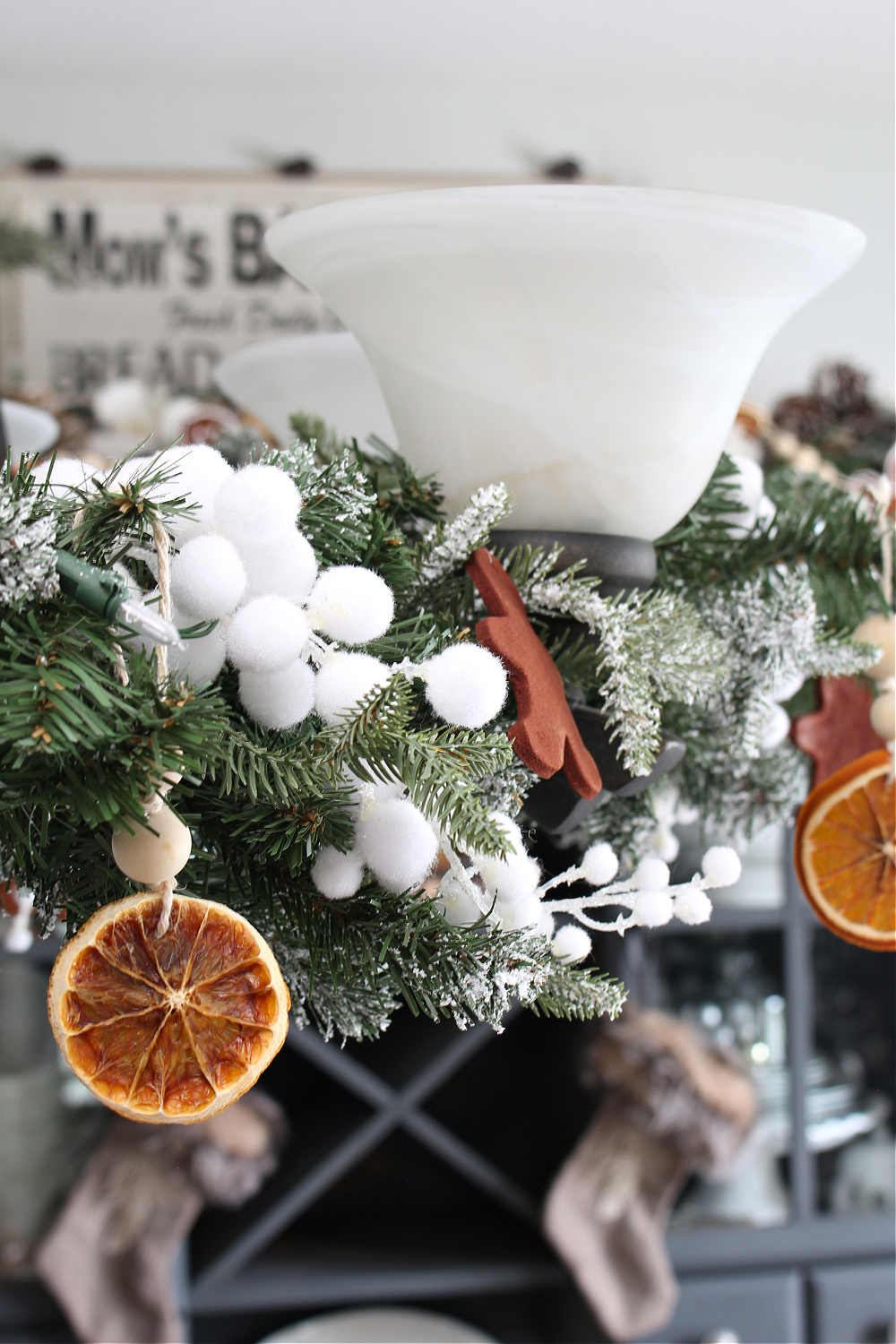LIght fixture in a dining room dressed up for Christmas with garland and dried oranges.