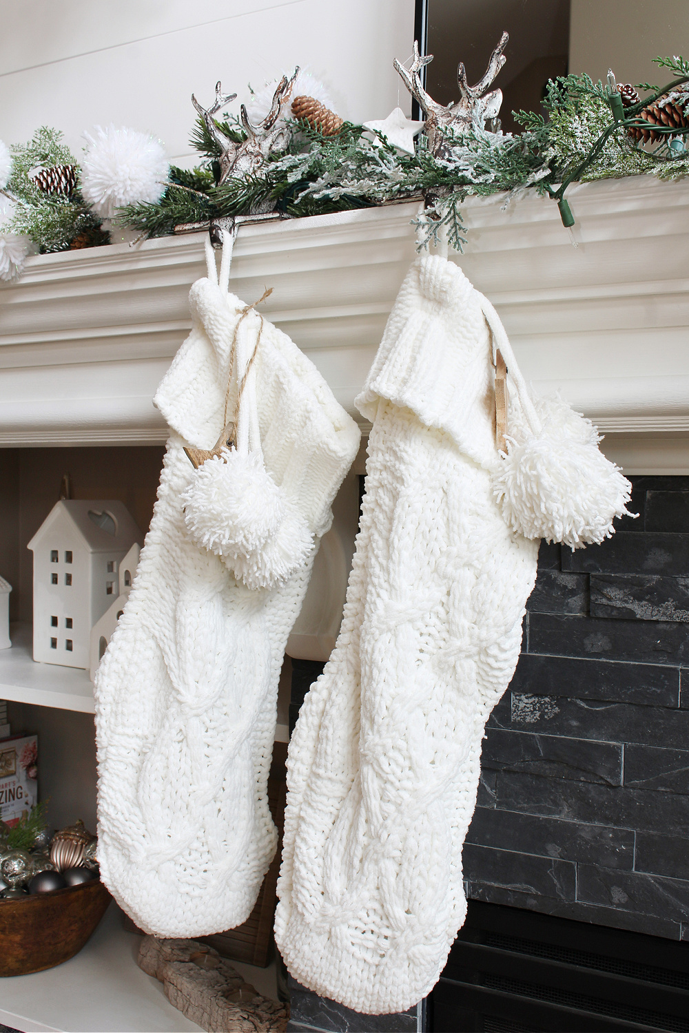 White knit Christmas stockings hung from a winter wonderland Christmas mantel.