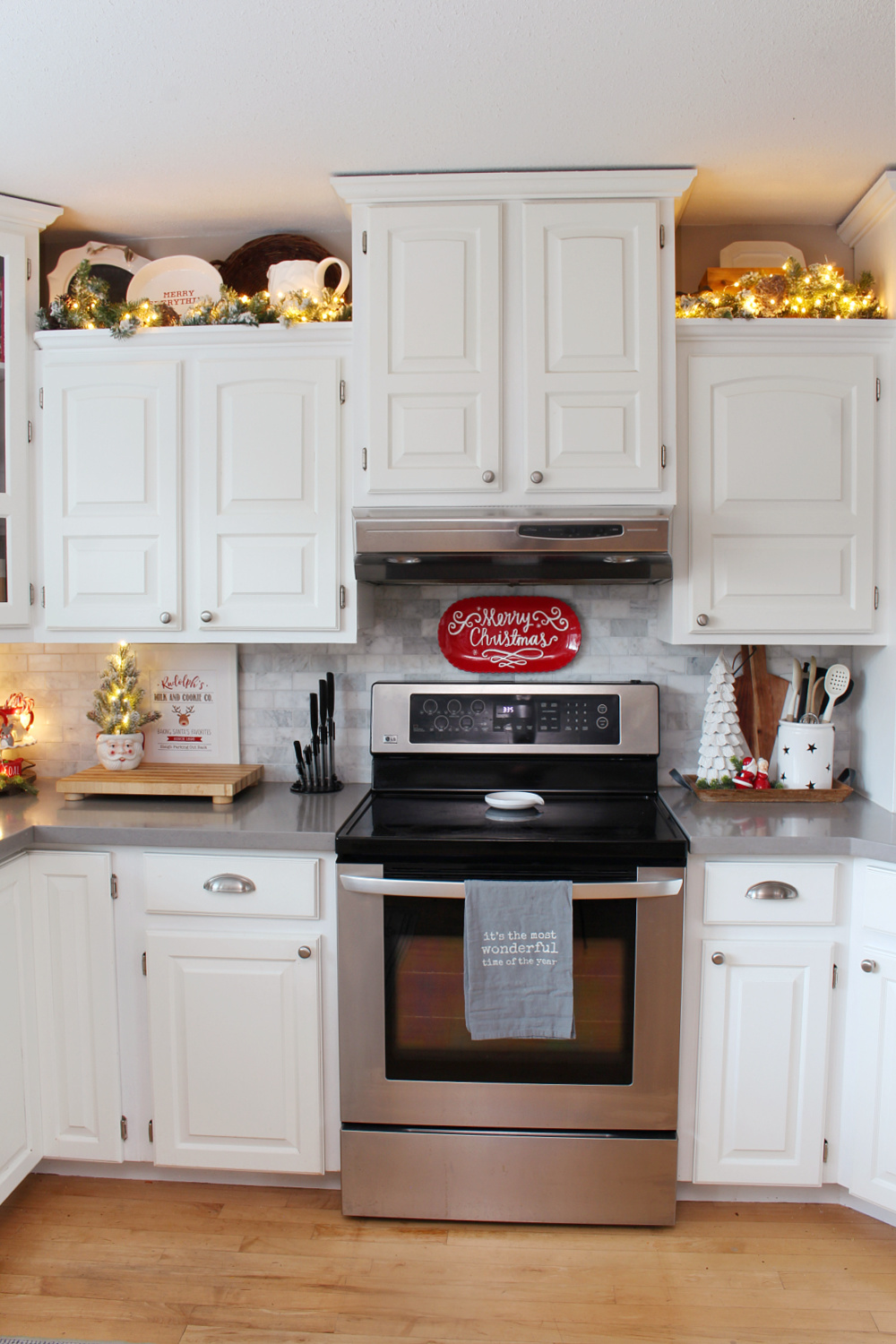 White kitchen decorated for Christmas with red and white decor with twinkle lights.