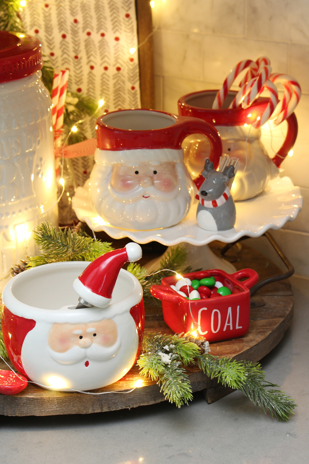 Red and white Christmas kitchen display with Santa mugs and twinkle lights.