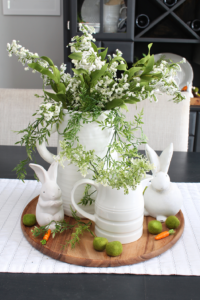 Simple spring centerpiece with white vases, greenery, and white bunnies.