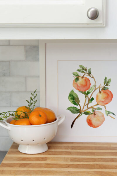 Tangerine art displayed in a white frame in a kitchen.