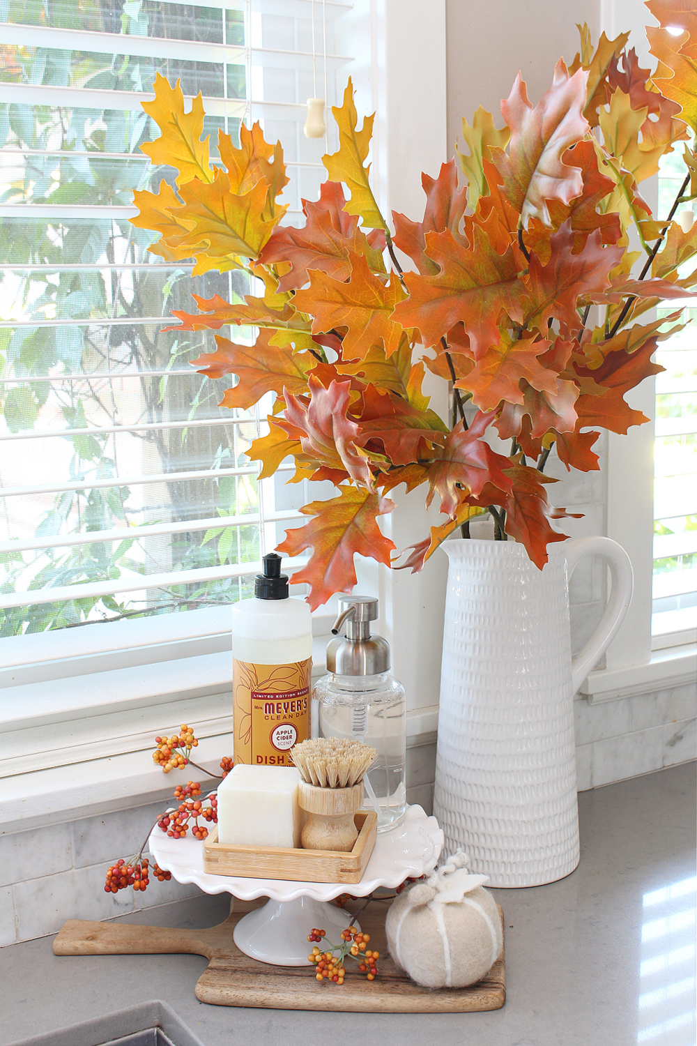 Fall kitchen sink display with cake stand, dish soaps, and oak leaves.